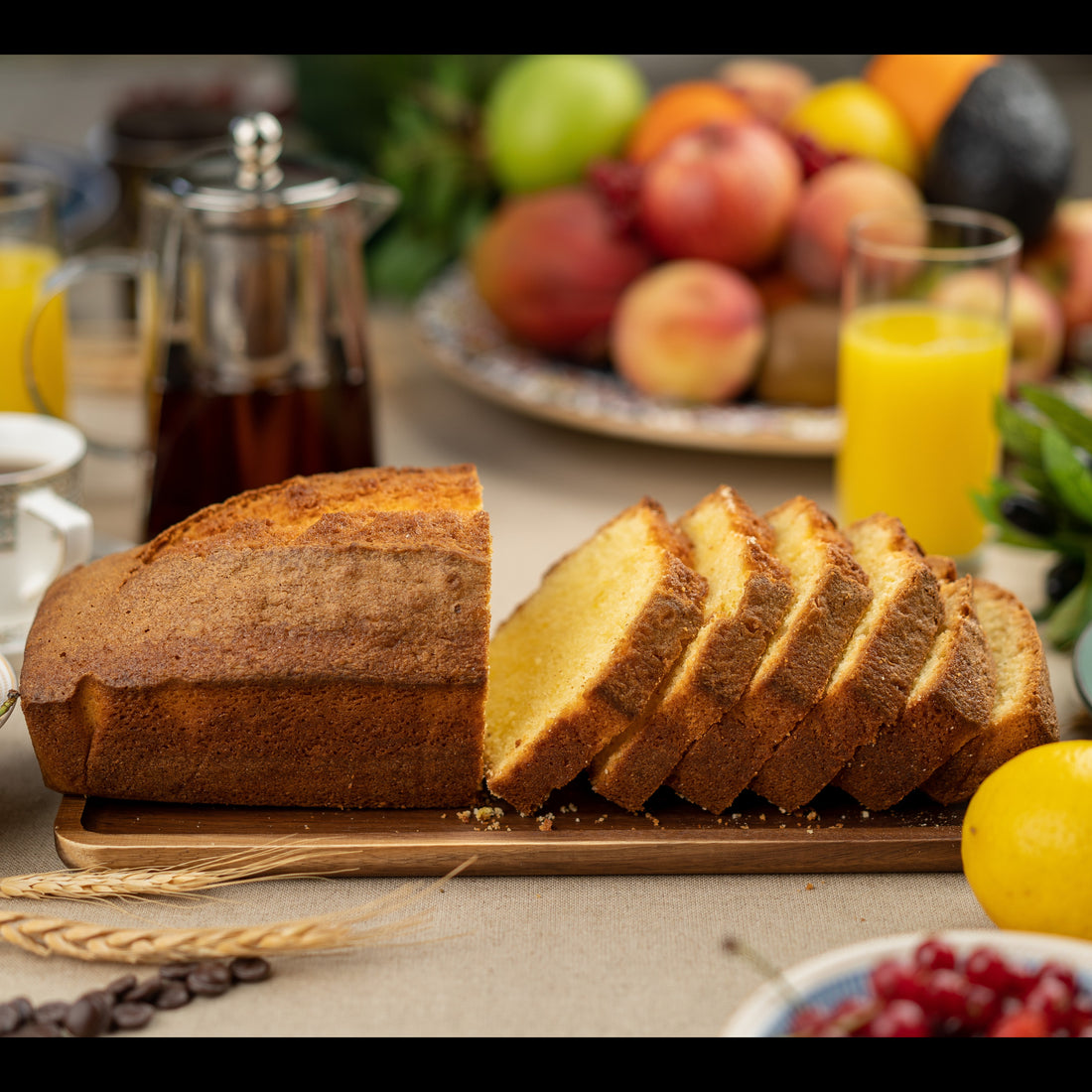 A wicker basket lined with a beige linen cloth, filled with assorted baked goods including a lemon cake and pastries on a wooden table in warm natural light.