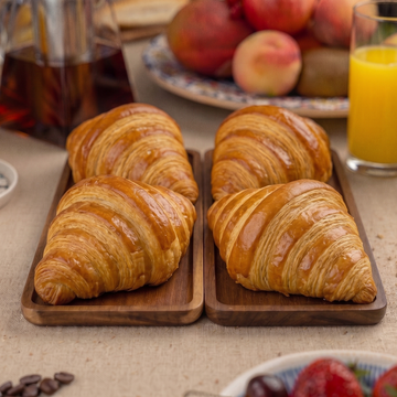 Wooden trays with croissants, coffee, and fruit on a table.
