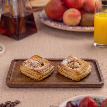 Two pastries on a wooden tray with a breakfast setting in the background.