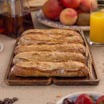 Tray of baguettes on a table with coffee, orange juice, and fruit.