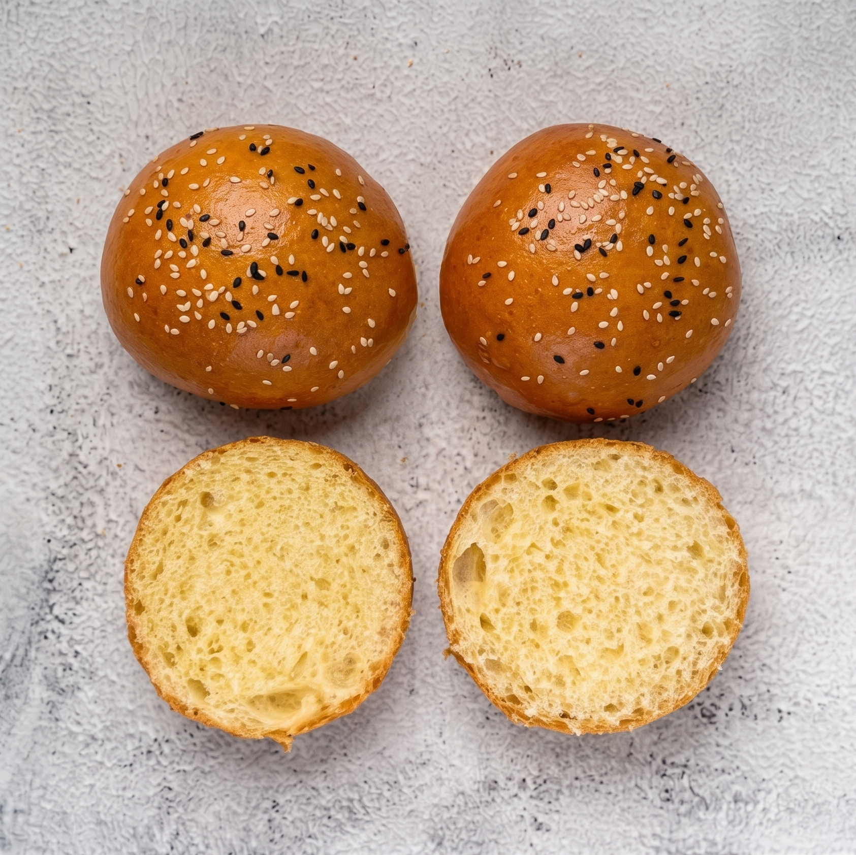 Four buns with sesame seeds on a textured surface